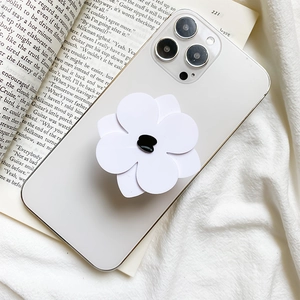 Minimalist white flower phone grip stand on a white smartphone in a cozy home setting