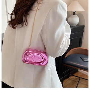 Détail d'un sac bandoulière rose miroir avec chaîne dorée sur un blazer blanc