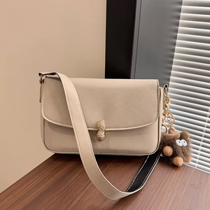 Cream square flap bag with gold peanut buckle and plush charm on a wooden desk