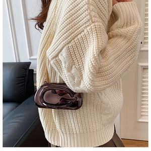 Porté croisé d'un sac en acrylique marron foncé brillant avec chaîne dorée sur pull