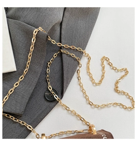 Detail of brown suede bag with gold chain strap and white stitching on grey fabric