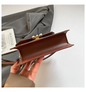 Gros plan d'un sac en cuir marron avec côtés accordéon et fermoir fleur en métal doré