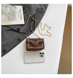 Detail of dark brown mini chain bag with white zigzag stitching next to a smartphone