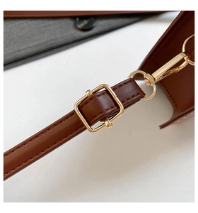 Détail d'une bandoulière en cuir marron avec boucle dorée et couture fine sur le sac