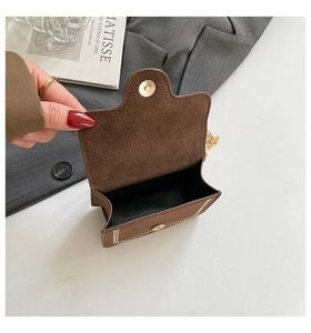 Close-up of brown suede mini bag with gold magnetic clasp, chain strap and white stitching