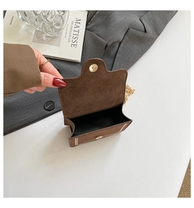 Detail of a brown suede mini bag with magnetic flap closure and golden chain strap