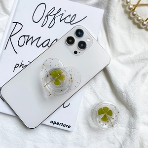 Collapsible gold foil four-leaf clover phone grip on a white smartphone back