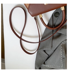 Détail d'un sac bandoulière en cuir marron avec une fine sangle d'épaule et poignée