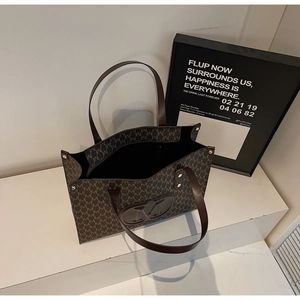 Detail of brown monogram tote bag with leather handles and round embossed logo on white stage