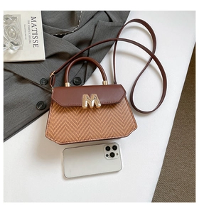 Détail d'un sac en cuir marron avec fermoir doré en M et téléphone pour comparer la taille