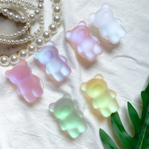 Vue à plat de supports de téléphone ours mats colorés sur tissu blanc avec perles et feuille