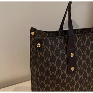 Close-up of vintage brown tote bag with M-pattern print and golden rivet detailing