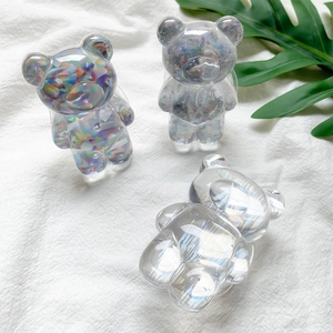 Detailed close-up of three bear-shaped resin phone grips on a white wrinkled fabric background