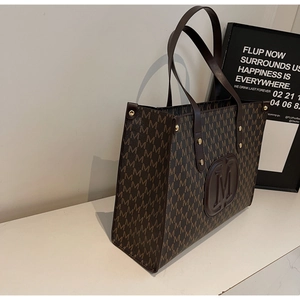 Detail of large tote bag in dark brown with M-pattern print and leather logo