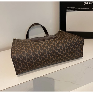 Detailed close-up of brown M-letter monogram pattern and leather logo on tote bag