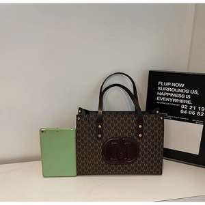 Detail view of large tote bag with M-letter monogram and brown leather handles