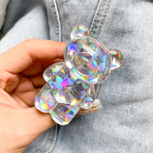Holographic 3D bear phone grip with iridescent geometric facets held over denim fabric