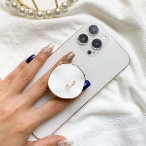 Detail view of a round white and gold LOVE phone grip on a white smartphone