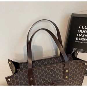 Close-up of brown tote bag with M-letter pattern, leather handles and gold metal rivets