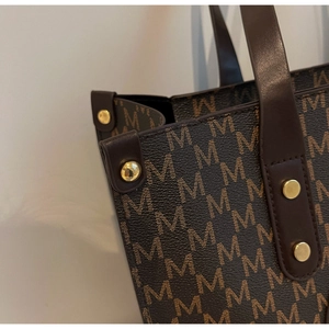 Detailed close-up of brown M-letter monogram tote bag with gold studs and pebbled leather