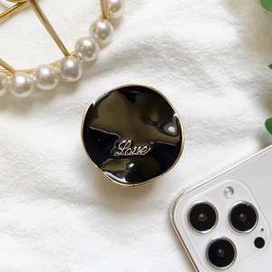 Close-up of black enamel phone grip with gold Love lettering and metallic trim
