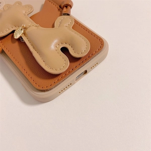 Détail d'une coque en cuir marron avec charme chiot beige et chaîne dorée pour smartphone