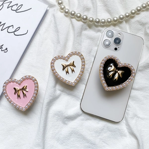 Pink white and black heart-shaped phone grip with pearl edges and golden bow design