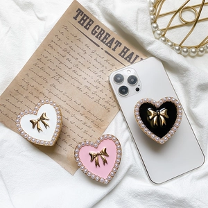Detail of heart-shaped phone stands with pearls and a 3D gold bow on a smartphone