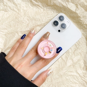 Pink donut phone grip with colorful sprinkles on white smartphone, beige textured backdrop