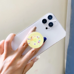 Detail showing a yellow donut phone grip with colorful sprinkles on a white smartphone