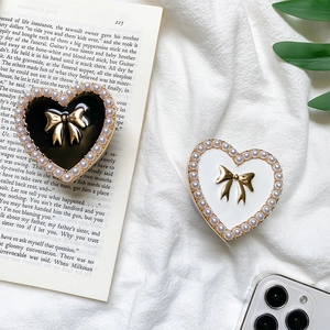 Detail of heart-shaped phone grips with pearls and golden bows on black and white surface
