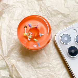 Macro shot of orange resin donut phone grip with colorful sprinkles on white background
