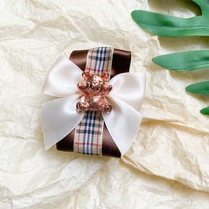 Close-up of plaid bow hair clip with a metallic bear charm on a cream textured background