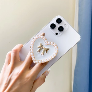 Detail view of a white heart-shaped phone grip with pearl trim and golden metal bow
