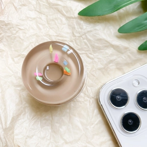 Macro shot of 3D donut phone grip with colorful sprinkles on beige paper background