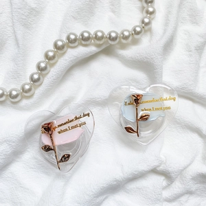 Close-up of heart-shaped phone stands with 3D metal roses on white fabric with pearls