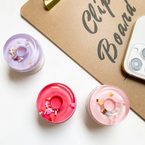 Close-up of pink, purple, and red 3D donut griptok set for smartphones on white surface