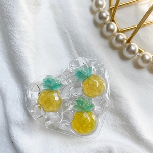 Detail of heart-shaped phone grip with embedded resin pineapples on a white textured background