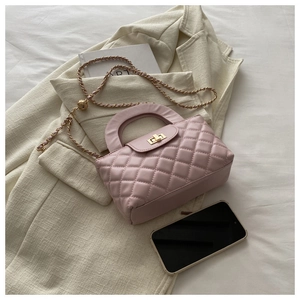 Detail of pink quilted leather shoulder bag with golden chain and twist lock on a neutral desk