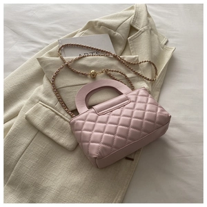 Detail of pink quilted leather handbag with gold chain strap on a white tweed jacket