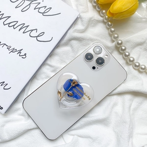 Detail showing a heart-shaped 3D blue rose phone grip on a white smartphone