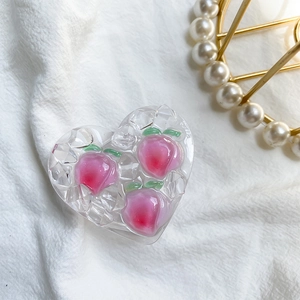 Detail of a heart-shaped clear phone socket with peach fruit charms and 3D crystal texture