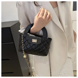 Detail of black quilted leather bag featuring gold twist lock and chain strap on a model