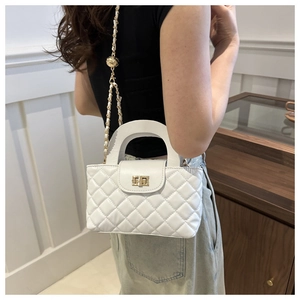 Close-up of white quilted handbag with golden ball chain and metallic twist lock
