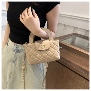 Close-up of beige quilted crossbody bag with gold turn-lock and ball chain detail