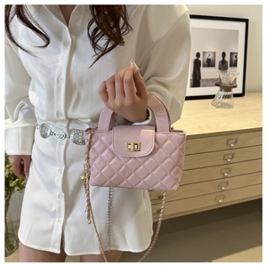 Close-up of pink quilted crossbody bag with gold turn-lock being held by a model