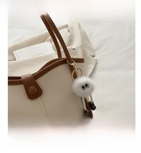 Detail of a cute white plush monster pendant with brown boots on a cream tote bag