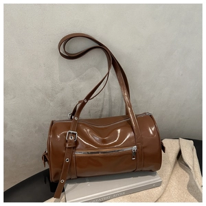 Close-up of brown glazed leather cylinder bag with adjustable strap and silver hardware
