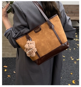Brown suede tote bag detail featuring embossed cat patterns and a cute plush bear charm