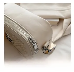 Detail of smooth silver zipper and textured beige synthetic leather on crossbody bag